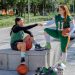 Two female athletes share a fist bump while sitting outdoors, holding sports equipment in Mexico City.